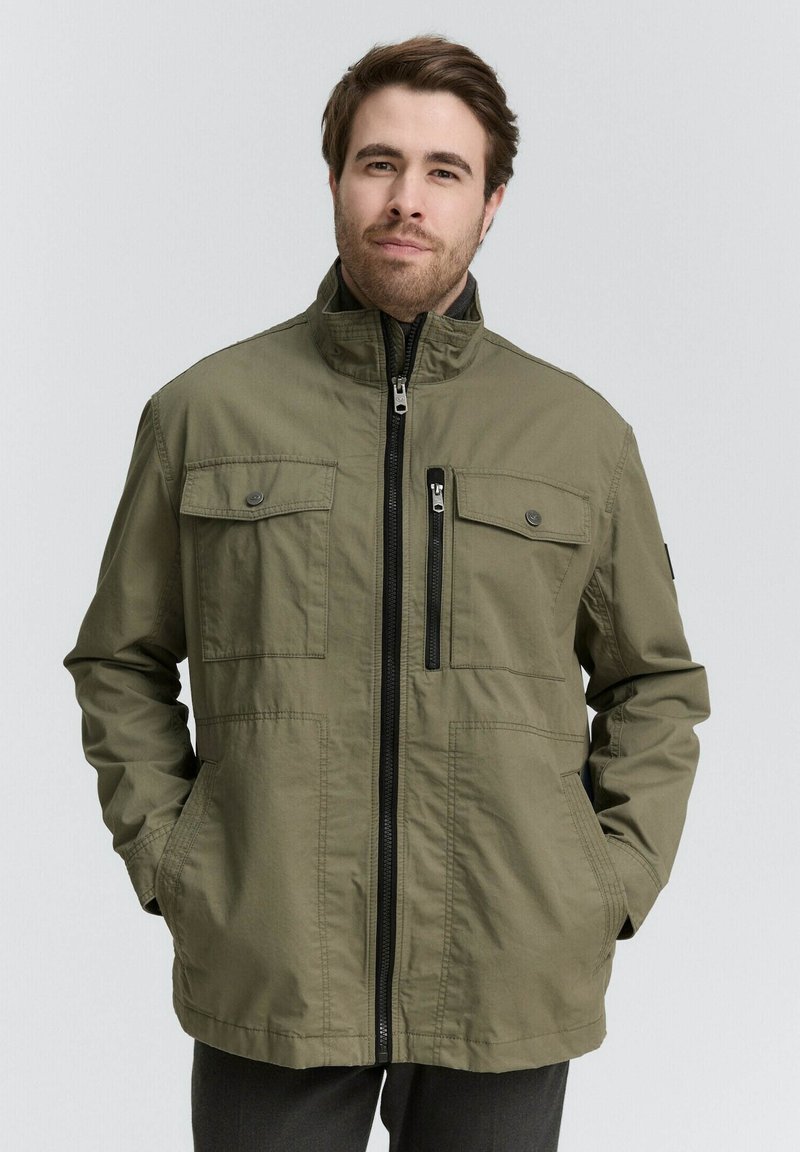 Olivgrüne Jacke mit einem hohen Kragen, Frontreißverschluss, mehreren Taschen und einer lässigen Passform. Der Stoff wirkt glatt mit minimalen Texturdetails.