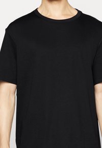 T-shirt nera con collo a giro in cotone morbido, caratterizzata da maniche corte e una vestibilità comoda, con una texture liscia e un design minimalista.