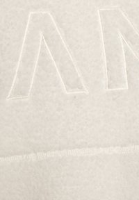 Elfenbeinfarbener Stoff mit weicher Textur und dezentem Muster. Er verfügt über ein erhabenes, geprägtes Design mit eckigen Formen. Nähte sind sichtbar.