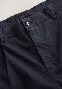Pantalon bleu marine foncé avec devant plat, doté d'une fermeture à un seul bouton, de passants pour ceinture et d'un tissu texturé. Étiquette de marque visible à l'intérieur.