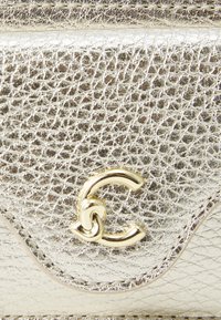 Sac à main en cuir doré métallique avec une surface texturée. Présente un logo doré décoratif et un design à rabat incurvé.