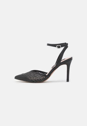Chaussure à talon haut noire avec bout pointu, détail en maille tissée et bride de cheville avec boucle sur fond blanc.