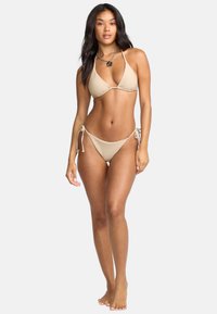 Beżowy bikini w kształcie trójkąta z regulowanymi wiązaniami w okolicy bioder i szyi, gładką teksturą, minimalistycznym designem i dopasowanym krojem.