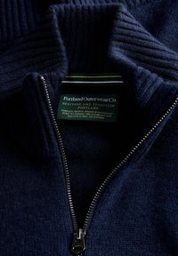 Granatowy sweter zapinany na zamek błyskawiczny z teksturowanym prążkowanym kołnierzem, zawierający metalowy zamek i metkę z napisem "Portland Outerwear Co."
