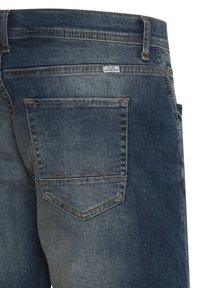 Vaqueros de denim en azul oscuro con una textura desgastada, que cuentan con dos bolsillos traseros, uno de ellos con un detalle de costura en zigzag y una etiqueta en la cinturilla.