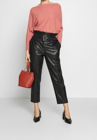 Maglione rosa a coste, pantaloni neri in pelle a vita alta, borsa rossa con manico ad anello, décolleté nere con punta a stiletto.