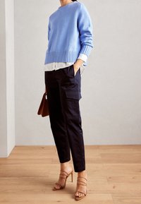 Lichtblauwe gebreide trui met ribbelrand, gedragen over een wit shirt. Gecombineerd met donkere cargobroek en beige strappy hakken. Bruine handtas.