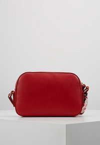 Punainen nahkainen olkalaukku, jossa on pyöreä muoto, sileä pinta, vetoketjullinen suljenta ja yksityiskohtia korostava kuviollinen remmi.