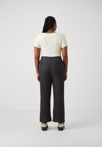 Cream ribbed short-sleeve top paired with dark patterned wide-leg trousers. The outfit is complemented by chunky green shoes with black soles.
