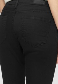 Jeans de mezclilla negra con una vista cercana del bolsillo trasero y la cinturilla. Presentan una textura suave y detalles de costura en contraste.
