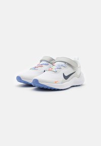 Zapatillas deportivas blancas con parte superior de malla, acentos grises, cordones multicolores y suela de goma azul. Presenta una banda de Velcro para el cierre.
