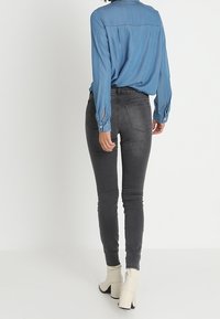 Pantalones vaqueros ajustados grises con bolsillos traseros, combinados con una camisa de mezclilla azul. La camisa tiene mangas largas y detalles de botones en los puños.
