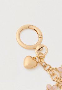 Kullatu melaniumnupp südamekujulisel ripatsil, millel on ahelalinke ja lilledega kaunistused. Sile pind ja läikiv viimistlus.