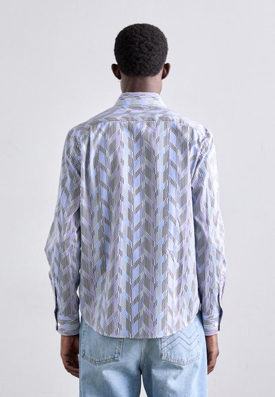 Camisa de manga larga con un patrón de zigzag en azul claro y blanco, cuello con botones y rayas en contraste en los puños y el dobladillo.