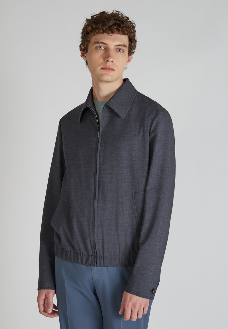 Ciemnoszara kurtka zapinana na zamek z usztywnionym kołnierzem, elastycznym paskiem w talii i ukrytymi kieszeniami po bokach, wykonana z teksturowanej tkaniny.