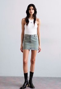 Fehér ujjatlan bodysuit, amelyet egy megkopott farmer mini szoknyával párosítottak. Fekete bokacsizma egészíti ki az öltözetet. Egyszerű dizájn, minimális részletekkel.