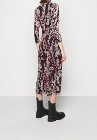 Kukkakuvioinen midi-mekko mustana, punaisena ja vaaleanpunaisena, jossa on pitkät hihat ja muotoiltu vyötärö. Yhdistetty mustiin nilkkabootseihin, joissa on teksturoitu pinta.