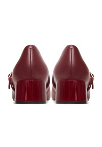 Burgundin väriset nahkakengät, joissa on tukeva korko ja sileä pinta. Ominaisuuksiin kuuluu erottuva kiiltävä korko ja sivussa oleva nauhalyöntti.