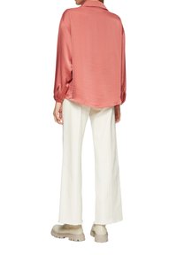 Chemise en satin rose clair avec col et manches longues, associée à un pantalon large blanc et des chaussures à semelle épaisse beige.