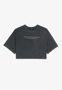 Grå cropped t-shirt lavet af blød bomuld. Har en rund halsudskæring og korteærmer. Teksten på forsiden siger: "BLIVER BEDRE OG VÆRRE PÅ SAMME TID."