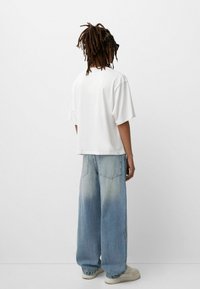 Weißes kurzärmliges T-Shirt, kombiniert mit lockeren hellblauen Denim-Jeans. Die Jeans haben ein verblasstes Design und eine klassische 5-Taschen-Anordnung.