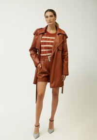 Brauner Kunstleder-Trenchcoat, taillierte Shorts und ein leichter gestreifter Pullover. Besitzt eine dekorative Gürtelsschnalle und glitzernde Absätze.