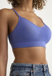 Lila bralette med tunna band, tillverkad av slät tyg. Har en sömlös design och ett brett, stötdämpande underband. Bärs med högmidjade jeans.