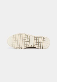 Sola di una scarpa con una superficie in gomma testurizzata beige, dotata di scanalature orizzontali e verticali per una migliore aderenza e durata.