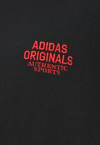 Μαύρο βαμβακερό t-shirt με κόκκινα κεντημένα γράμματα: «ADIDAS ORIGINALS AUTHENTIC SPORTS» εμφανώς στο κέντρο.