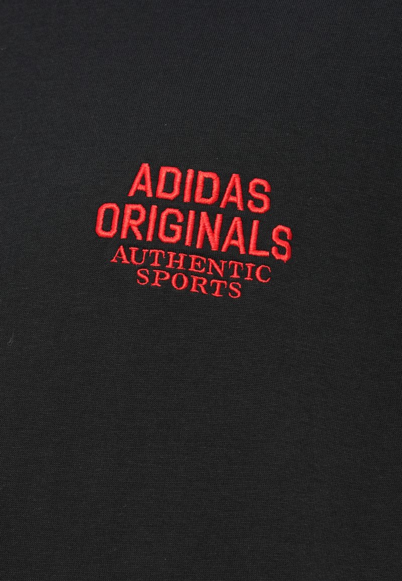 T-shirt noir en coton, avec un texte rouge brodé : "ADIDAS ORIGINALS AUTHENTIC SPORTS" affiché en évidence au centre.