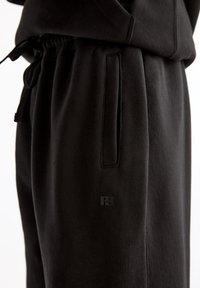 Zwarte sweatpants gemaakt van zachte stof, met een trekkoord in de taille, zijzakken en een subtiele ingedrukte logo op de linker dij.
