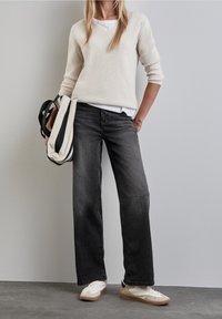 Suéter de punto beige, camiseta blanca debajo, jeans negros de pierna ancha y zapatillas crema con acentos beige. Bolsa a rayas en blanco y negro.