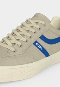 Baskets en daim beige avec des lacets crème, une bande latérale bleue étiquetée « BOSS » et une semelle en caoutchouc écru texturée.