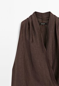 Top avvolgente in lino marrone con una finitura testurizzata, caratterizzato da un profondo scollo a V e un design minimalista. Etichetta visibile all'collo.