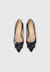 Schwarze Lackleder Ballerinas mit spitzem Zehenbereich, die mit einer dekorativen Perlenakzentuierung an der Vorderseite versehen sind. Weiche beige Innenauskleidung und dezentes Logodetail.