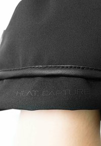Zwarte stof met een gladde textuur, met een gestikte rand. De ingedrukte tekst "HEAT CAPTURE SYSTEM" is zichtbaar nabij de onderkant.
