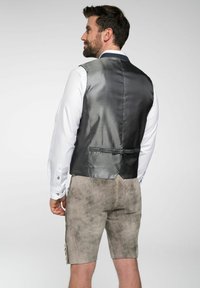 Grahamuster-Weste mit satinierter Oberfläche, kombiniert mit einem weißen Langarmshirt. Auch graue Shorts mit strukturiertem Look sind enthalten.