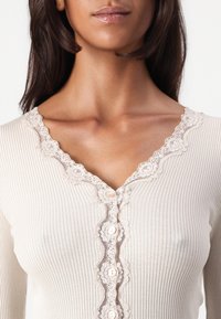 Ribbed beige top featuring a V-neck with delicate lace trim, decorative buttons down the front, and a soft, textured fabric.