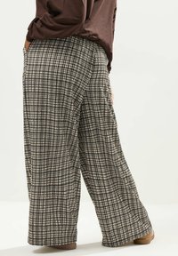 Vida-byxor i svart och krämfärgad rutmönster, med en texturerad tygkvalitet och sidofickor, ihop med en brun topp.