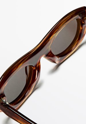 Braune Schildpatt-Sonnenbrille mit runden Rahmen, dunklen Gläsern und glänzender Oberfläche, die dicke, kurvige Bügel und minimale Beschläge präsentiert.