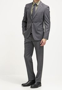 Grau maßgeschneiderter Anzug mit schlanker Passform, kombiniert mit einem grünen Hemd, passender Krawatte und schwarzen Lederschuhen. Glatte Textur, minimales Muster.