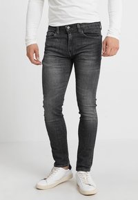 Jeans ajustados de mezclilla gris oscuro, con un diseño clásico de cinco bolsillos, sutiles desgastes y combinados con zapatillas blancas.
