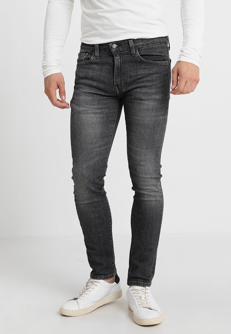 Jeans ajustados de mezclilla gris oscuro, con un diseño clásico de cinco bolsillos, sutiles desgastes y combinados con zapatillas blancas.