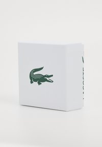 White rectangular box made of textured material featuring a green crocodile logo and brand name on the side.
