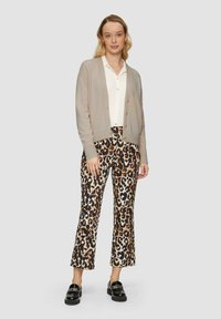 Hellgrauer Cardigan mit Knopfverschluss, kombiniert mit hoch taillierten, leopardgemusterten Schlaghosen. Das Model trägt schwarze Schuhe. Minimalistischer Hintergrund.