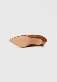 Chaussure à talon haut en suede marron avec un bout pointu et une semelle lisse de couleur nude. La chaussure présente des plis subtils le long de la tige.