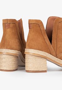 Botas de tobillo de ante marrón con lados recortados y un tacón de bloque envuelto en yute texturizado, con acentos de cuero para un detalle adicional.