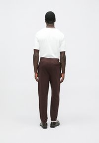 Bordó színű melegítőnadrág rugalmas derékpánttal, leszűkített szárakkal és oldalzsebekkel, sima fehér pólóval párosítva.