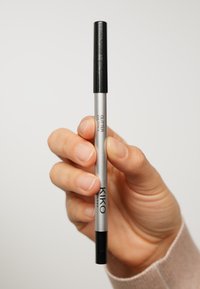 Crayon eye glitter KIKO avec un corps argenté et un capuchon noir, présentant une forme élancée et une texture lisse, tenu entre les doigts.
