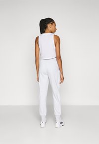 Top corto sin mangas blanco y joggers gris claro, con puños elásticos y bolsillos laterales. Completado con zapatillas deportivas blancas con detalles en negro.